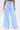 Wearing the ASHLEY RELAXED PANT, a high-rise, wide-leg style in light blue pinstripes with a drawstring waist, paired with white heeled sandals and a small white handbag against a plain background.