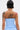 A person with short dark hair, shown from the back, wears the ASHLEY BRALETTE in light blue with subtle pin stripes. Their upper back and arms display several tattoos, including a portrait, a handprint, and a snake.