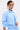 A person with slicked-back short hair and large floral earrings poses confidently against a white background in the light blue, cotton-blend ASHLEY BUTTON DOWN TOP featuring smocked and ruffled details.