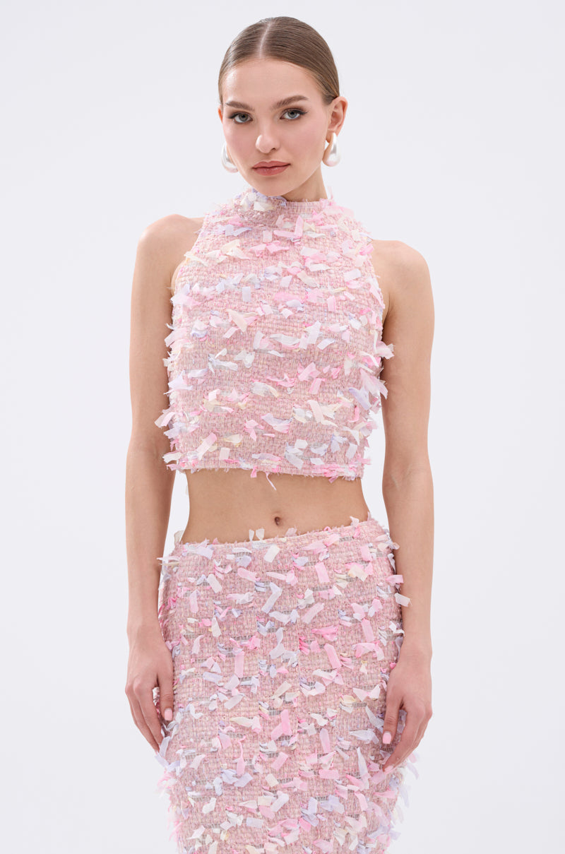 A woman wears the WILD AND FREE FRINGE BLOUSE—a sleeveless, pastel pink cropped top with fringe and applique details—paired with a matching skirt, standing against a white background. Playful pastel fringe detailing stands out.
