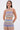 A woman with long brown hair wears the TAKE ME TO MIAMI HALTER TOP and matching pants, showcasing a retro-inspired wavy striped pattern in red, blue, green, and beige. She stands against a plain white background.