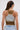 A woman with long brown hair in a ponytail, wearing glasses and the MOST WANTED TANK in brown and gray, paired with light blue jeans, is pictured from the back against a plain light background.