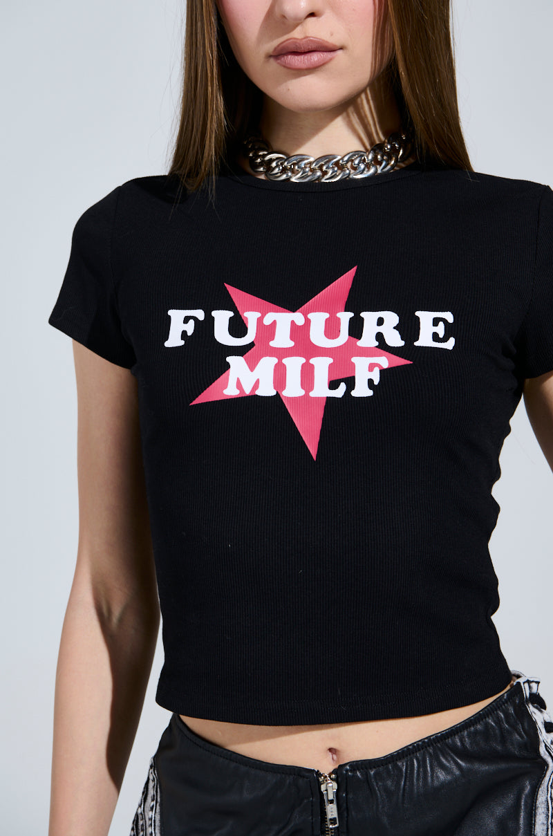 A person in a FUTURE MILF BABY TEE, featuring a red star and "Future MILF" text on black ribbed knit, pairs it with black pants with zippers. Their long brown hair adds flair to the chunky chain necklace, completing an edgy look. 5