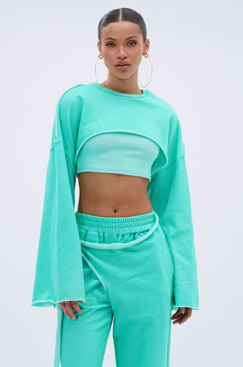 Woman wearing the ISSA DOUBLE LAYER CROP SWEATSHIRT IN TIFFANY, paired with matching wide-leg pants. Her hair is styled back, she wears hoop earrings, and the background is light and plain. 1