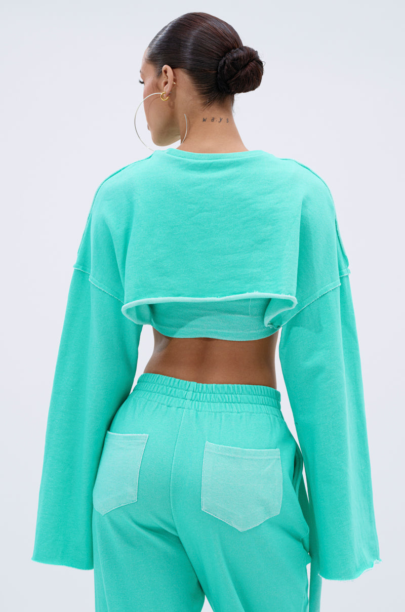 A woman with slicked-back hair in a bun wears hoop earrings and the ISSA DOUBLE LAYER CROP SWEATSHIRT IN TIFFANY with matching high-waisted loungewear pants, seen from the back. 3