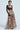 A person poses confidently in a sheer black lace top and the ALL I NEED METALLIC MAXI CARGO SKIRT. With short hair and a statement choker, they stand against a plain light blue backdrop, adding striking contrast to the high-rise design ensemble.