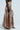 A person in a black lace top and the "All I Need Metallic Maxi Cargo Skirt" with pockets and flowing design, paired with open-toed black heels against a plain light gray background that highlights the ensemble's sophisticated metallic fabric.