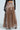 A person in the ALL I NEED METALLIC MAXI CARGO SKIRT, a bronze-colored, metallic fabric maxi skirt, paired with sheer black lace gloves, stands against a neutral background.