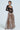 A person poses in a fashion-forward outfit, featuring a black lace top with intricate patterns and the ALL I NEED METALLIC MAXI CARGO SKIRT, complete with large pockets. The ensemble includes a choker necklace for a stylish touch against a plain background.