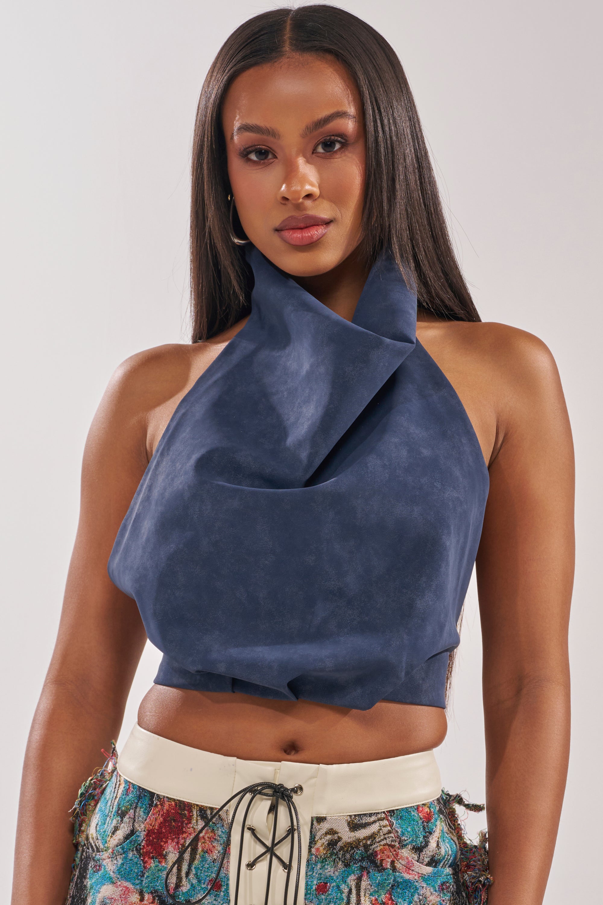 A woman with long straight hair wears the JANE SUEDE HALTER TOP in navy blue and cream-colored pants with colorful patterns, standing facing forward against a plain background. 1