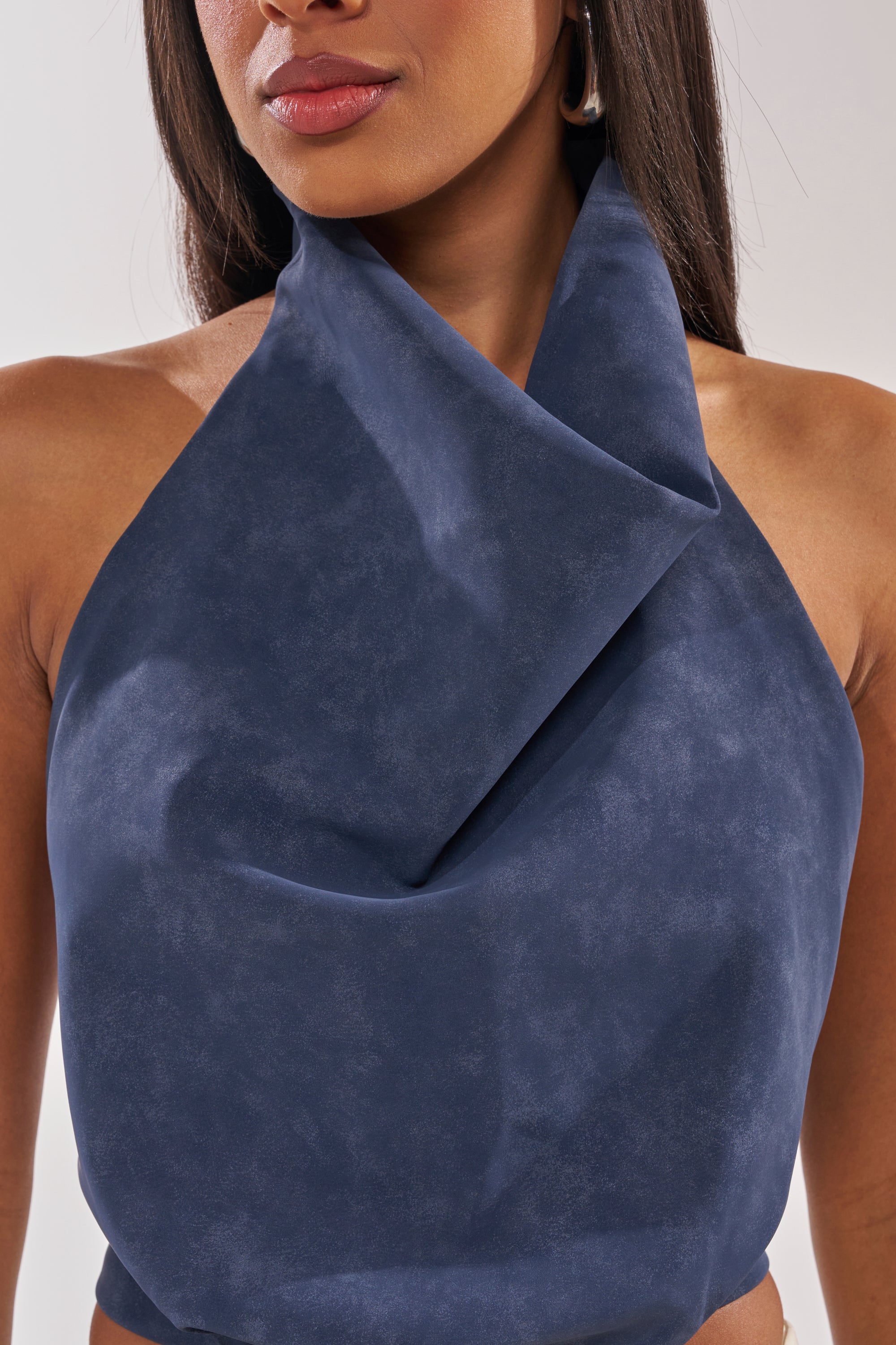 A woman wears the JANE SUEDE HALTER TOP, a sleeveless navy blue halter with a draped front and fold-over neckline. Only her mouth, chin, and upper torso are shown. 6