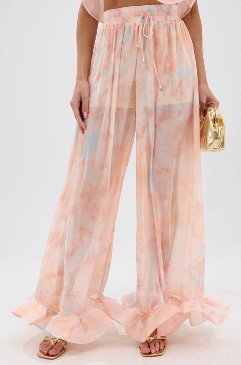A person wears the COLORFUL SKY OMBRE PALAZZO PANT—high-rise, wide-leg with ruffled hems—paired with sandals and a small gold handbag; image cropped above the chest. 1