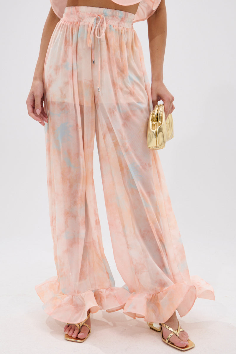 A person wearing the COLORFUL SKY OMBRE PALAZZO PANT with high-rise wide legs, ruffled hems, a matching crop top, gold sandals, and holding a small gold handbag against a plain white background. 2