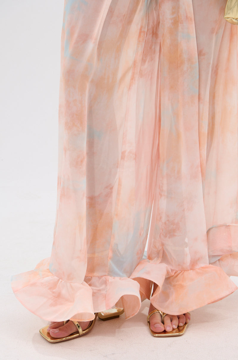 A close-up of the COLORFUL SKY OMBRE PALAZZO PANT, featuring sheer fabric in peach, blue, and pink with ruffled hems and a high-rise wide-leg cut, styled with metallic gold sandals against a white background. 7