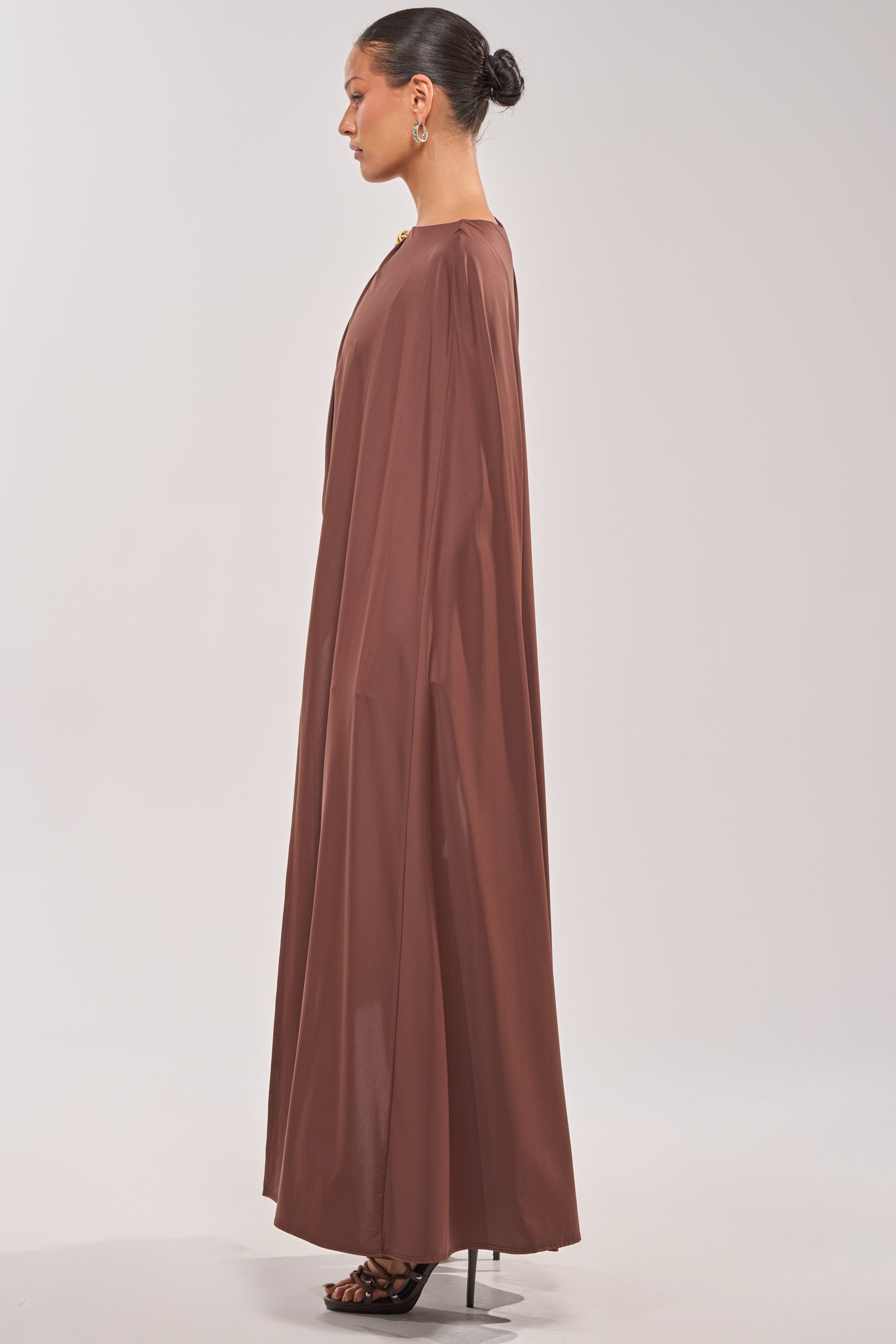 A woman poses in profile against a plain, light background, wearing the NOT YOURS CAPE BODYSUIT. She pairs it with loose sleeves, high heels, and has her hair styled in a neat bun for an editorial look. 4