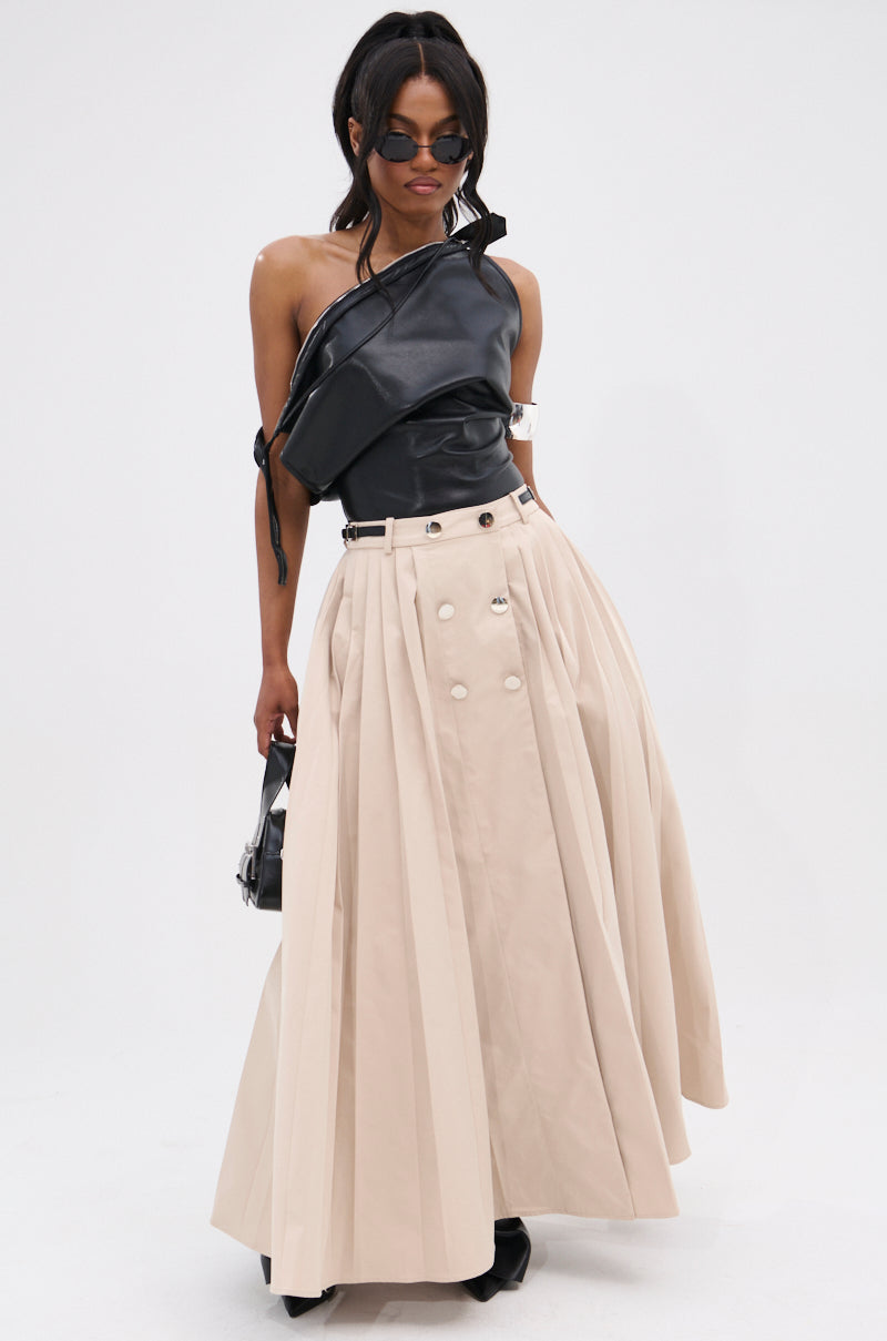 A woman in sunglasses models the WEEKEND VIBES FAUX LEATHER BLOUSE, styled off-the-shoulder with a high-waisted beige pleated maxi skirt featuring button details. She holds a small black handbag against a plain white background.