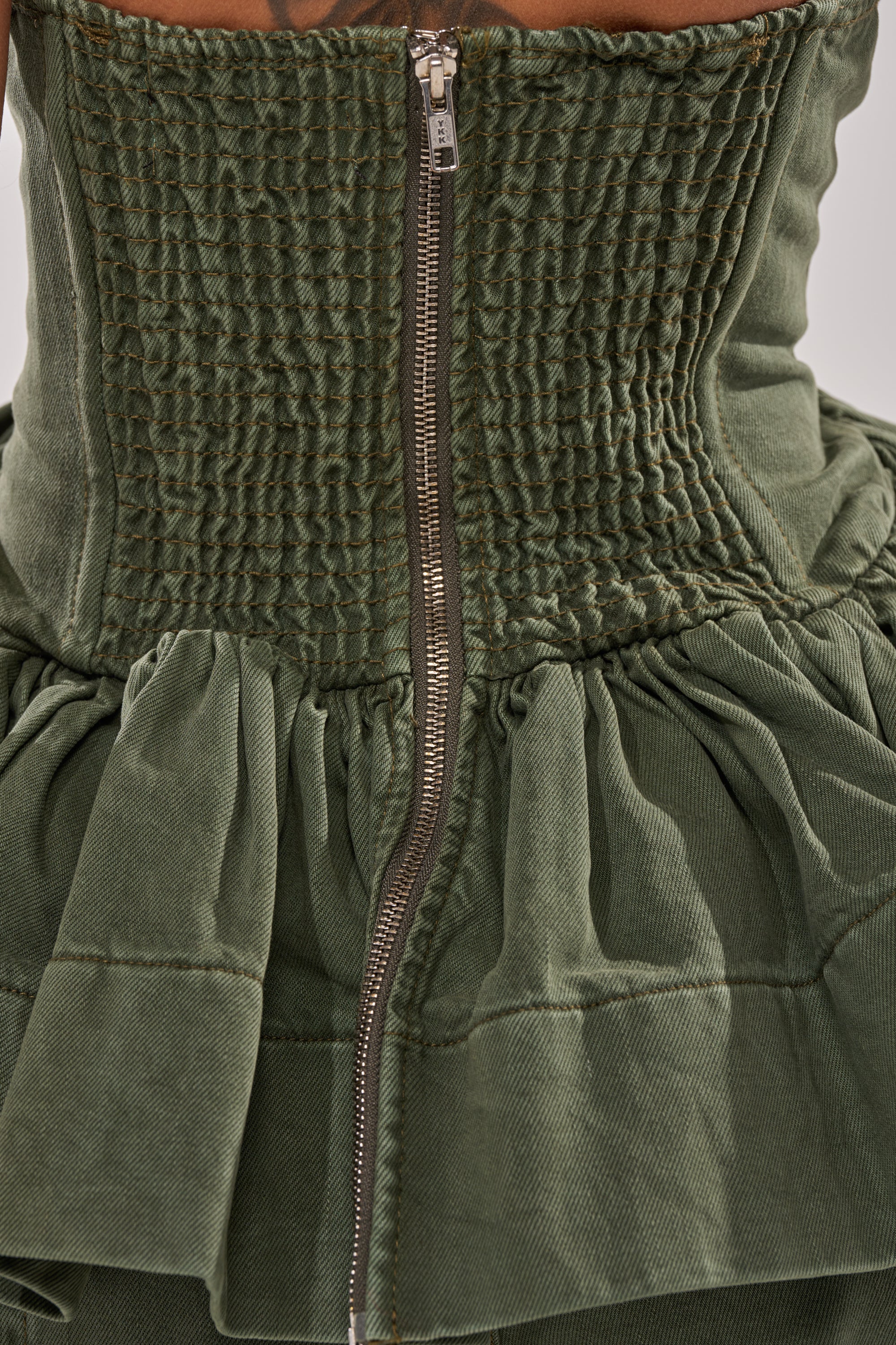 Close-up of the back of the KARA DENIM CORSET in green, showing a textured, ruched smocked bodice with a silver center zipper and a gathered, ruffled skirt. 7