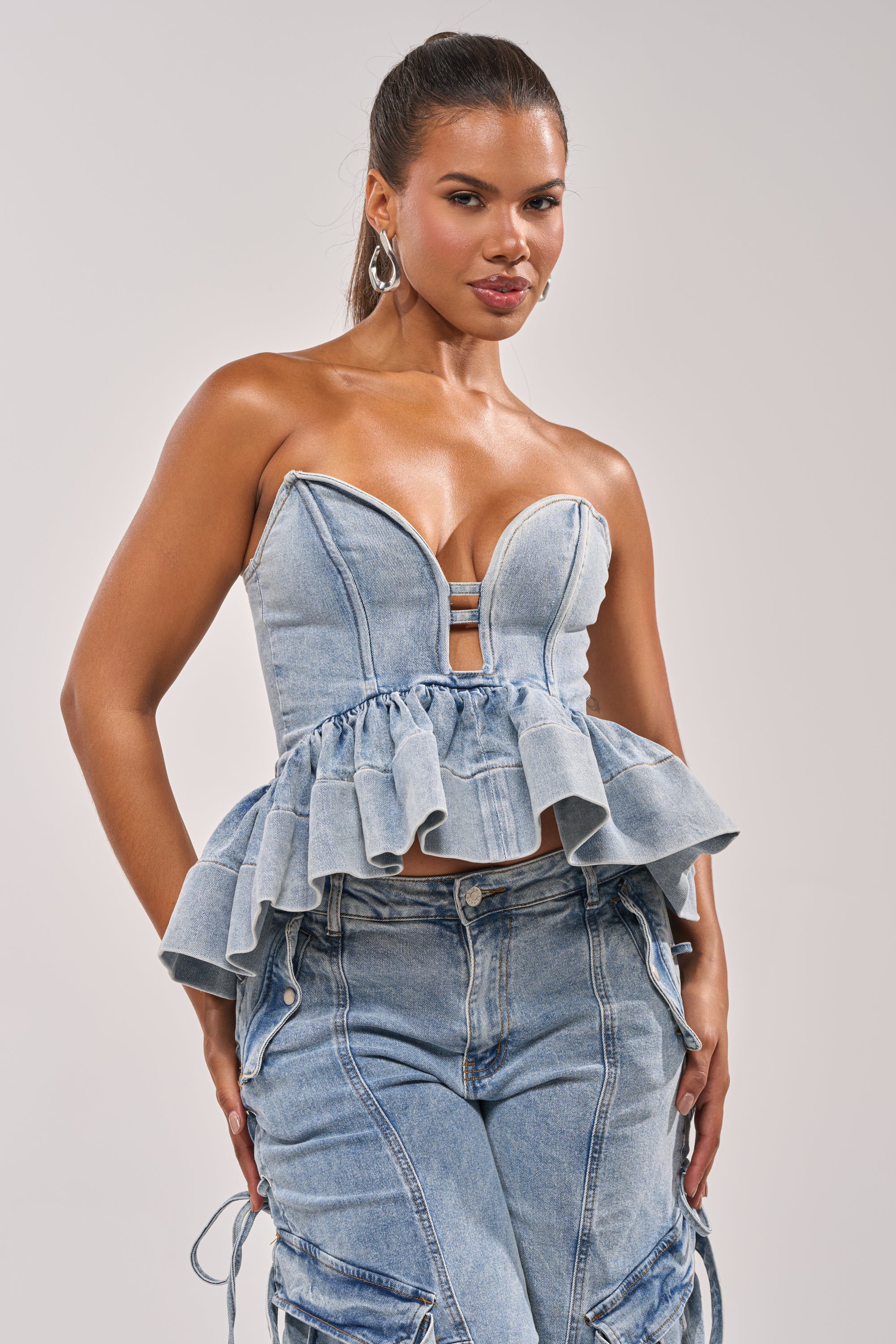 A woman poses confidently in the KARA DENIM BLOUSE paired with matching high-waisted jeans featuring side ties, creating a chic festival outfit against a plain light background. 0