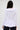 A person with long dark hair is shown from the back wearing the RENAISSANCE RUFFLE DETAIL BLOUSE, featuring ruffles on the collar, hem, and cuffs, paired with dark pants against a plain light background.