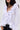 A woman wears the RENAISSANCE RUFFLE DETAIL BLOUSE—a long-sleeved white top with dramatic ruffles along the deep V-neck and hem—paired with dark jeans. Her dark hair is down, finishing the elegant look.