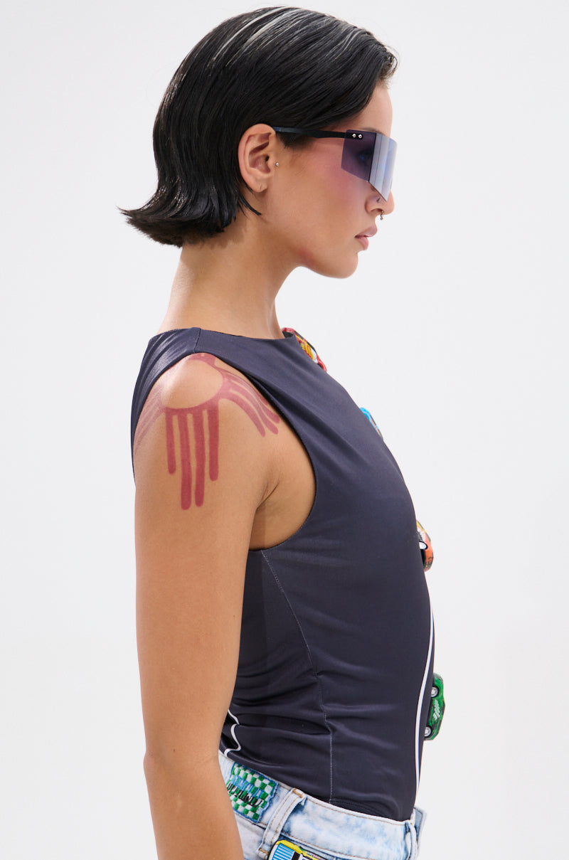 A person with short dark hair and futuristic sunglasses is shown in profile wearing the FINISH LINE BODYSUIT, a curve-hugging sleeveless dark top, paired with light denim jeans. A red race track graphic decorates their upper arm.