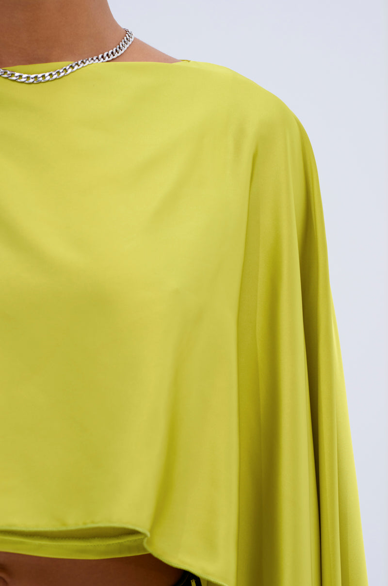 A person wears a shiny silver chain necklace and the COCKTAIL HOUR BLOUSE IN CHARTREUSE, a bright satin blouse; only their neck, shoulders, and upper torso are visible against a plain light background.