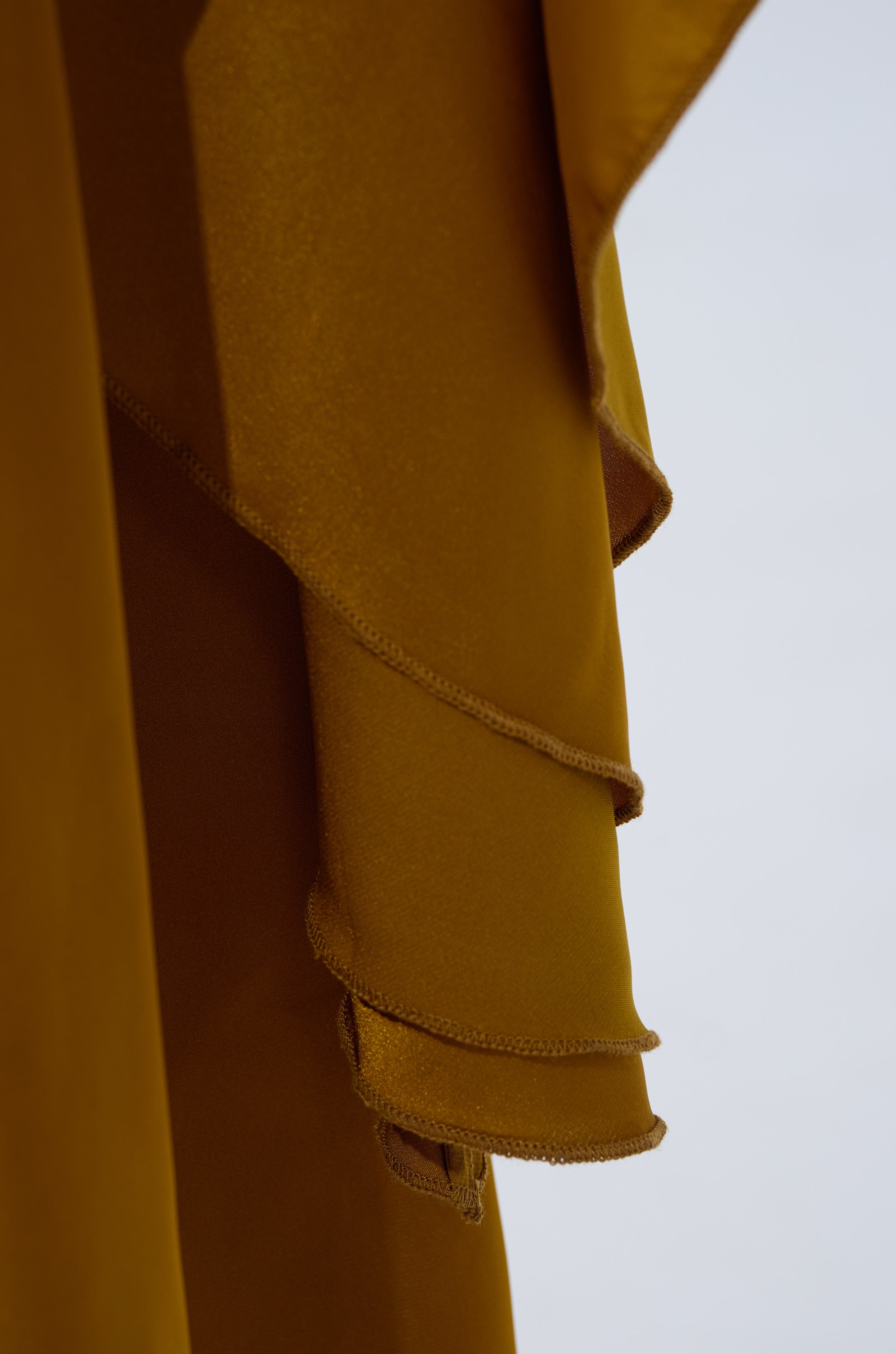 A close-up of the COCKTAIL HOUR BLOUSE IN MUSTARD shows silky satin-like fabric with stitched edges, draped in soft folds against a light, blurred background.