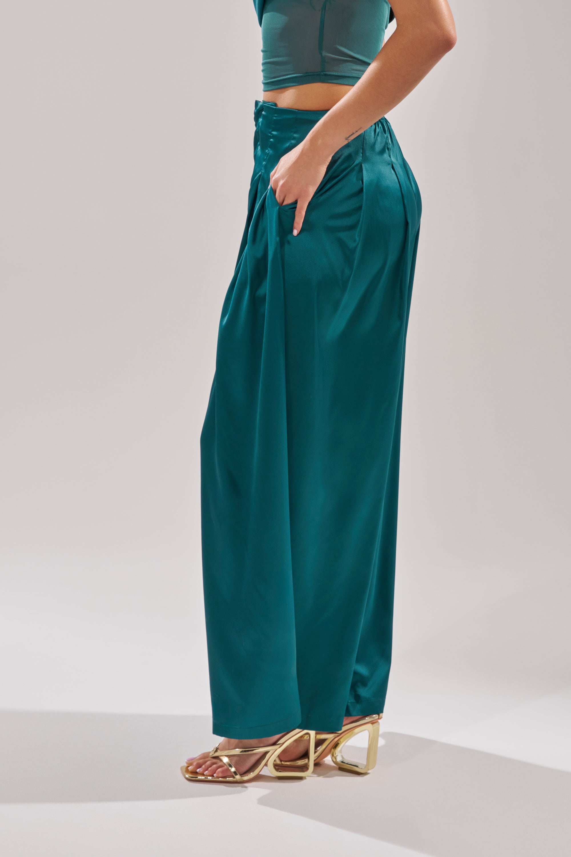 A person stands against a plain light background wearing GIRLS FOR LIFE EMERALD TROUSER, a matching teal crop top, and gold open-toe heeled sandals. 3