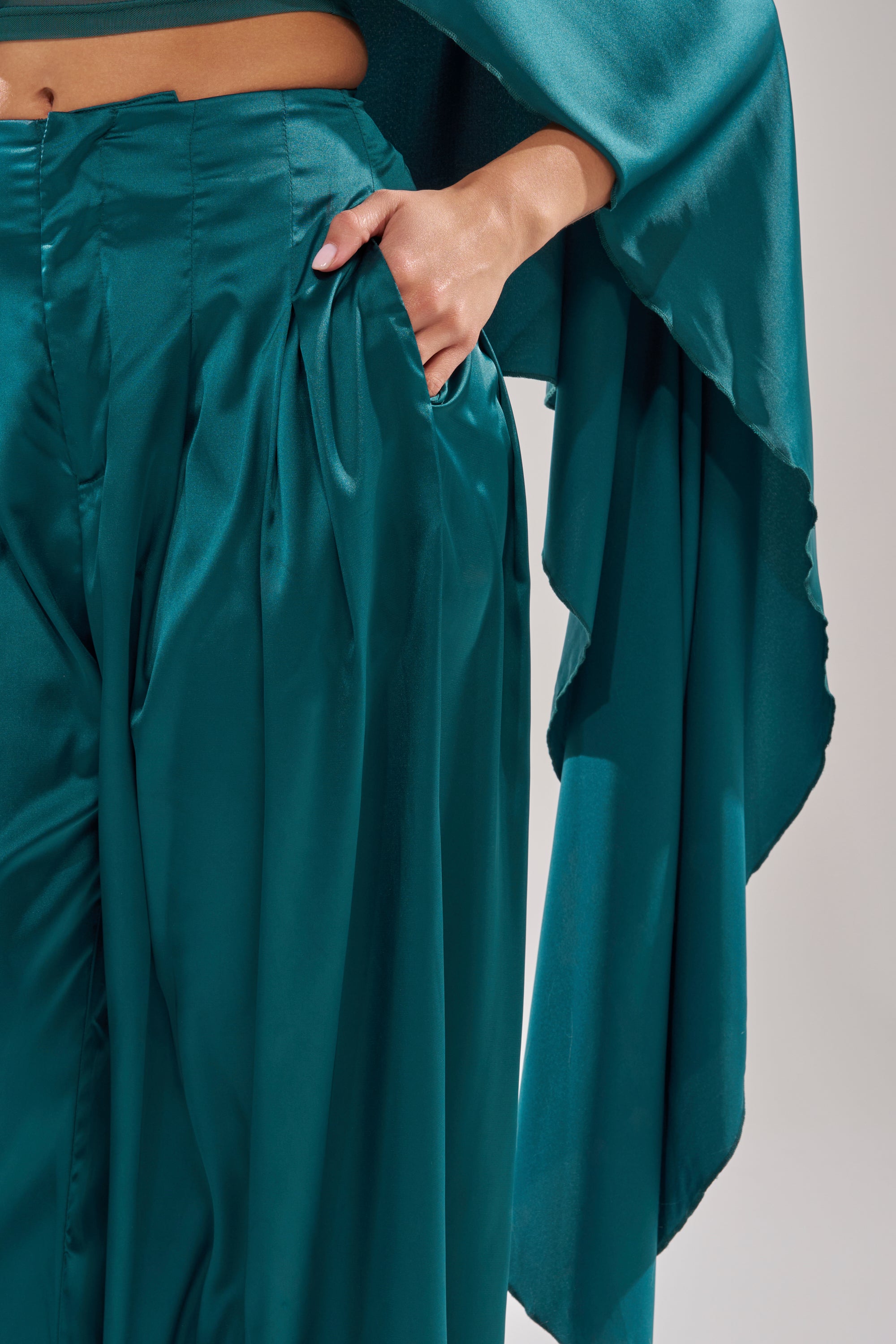 A person wearing the GIRLS FOR LIFE EMERALD TROUSER and a matching flowing top poses with one hand in their pocket, highlighting the outfit's glossy, smooth texture. 7