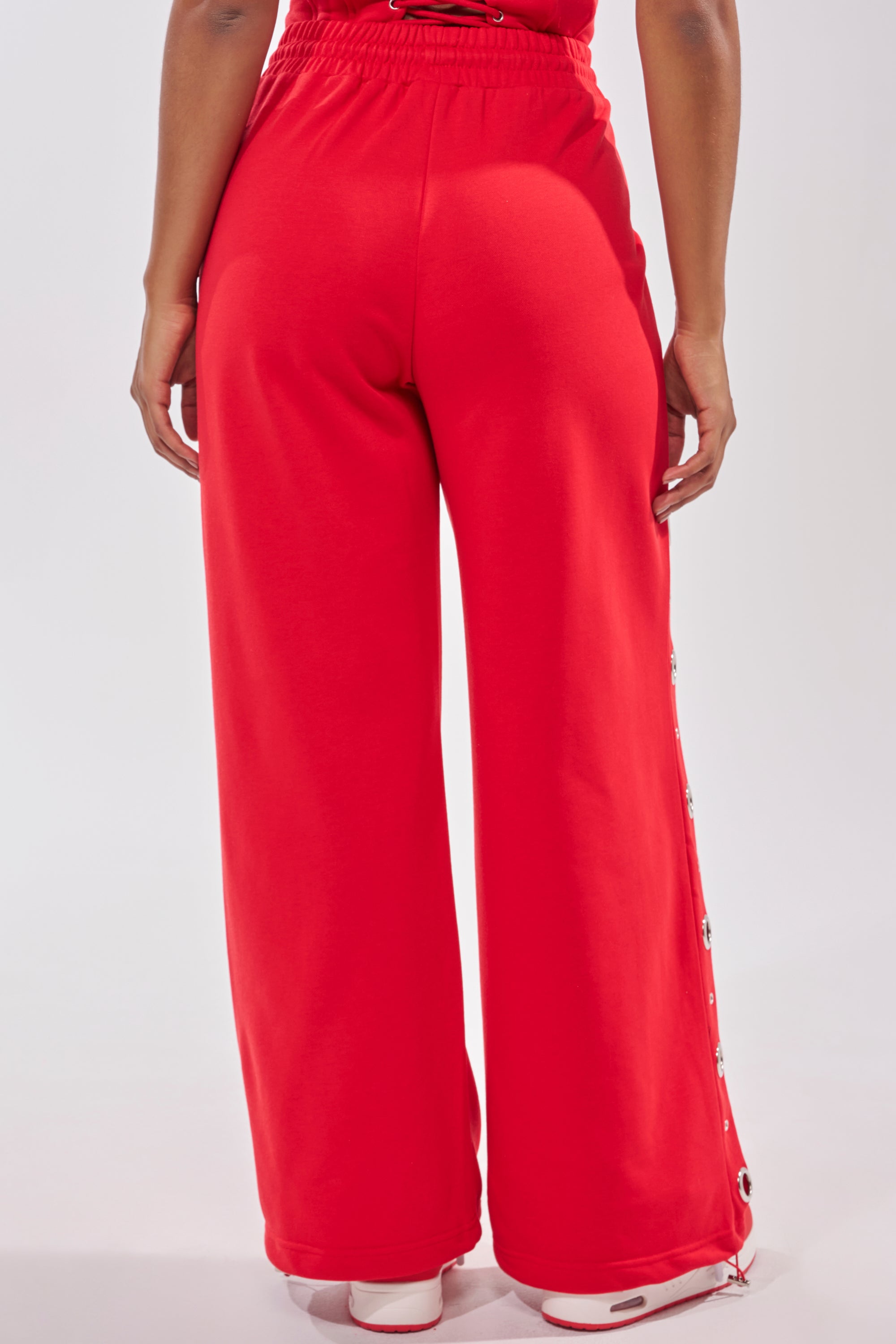 A person is shown from the back wearing COMFY COZY SWEATPANT in red with side button details, paired with a matching top and white sneakers, set against a plain light background. 6