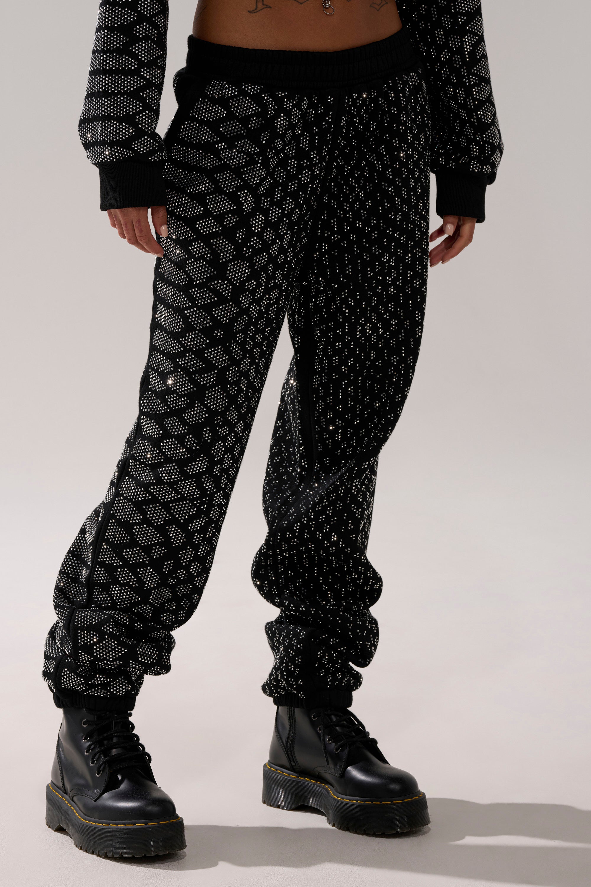 A person models the SNEAKY LITTLE SNAKE WIDE LEG JOGGER with a white dotted geometric pattern and matching top, paired with black lace-up boots, standing against a light background. Their face is not shown.