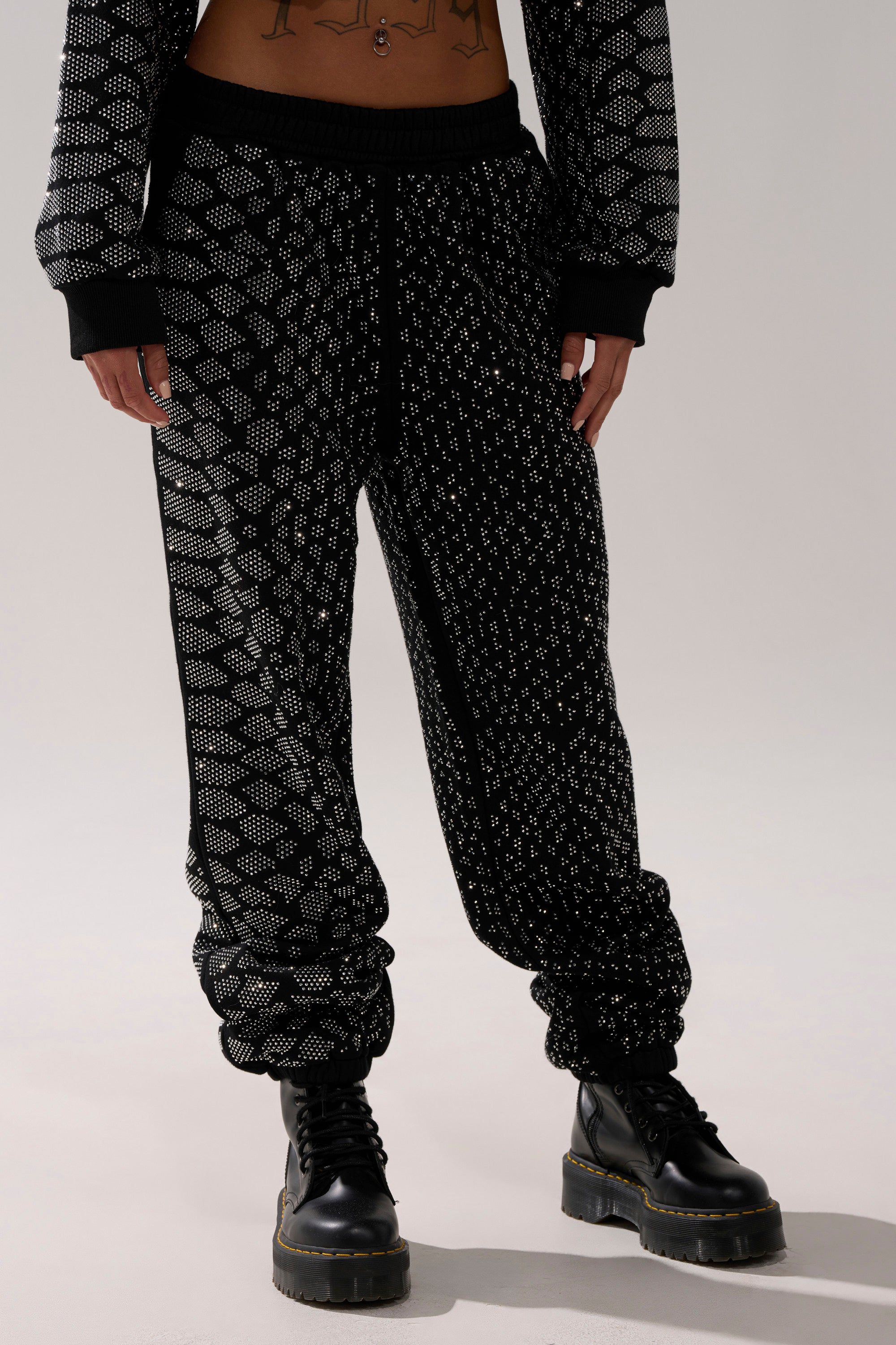 A person wearing the SNEAKY LITTLE SNAKE WIDE LEG JOGGER, featuring a black design with a white geometric pattern, pairs it with black lace-up combat boots while standing against a plain light background.