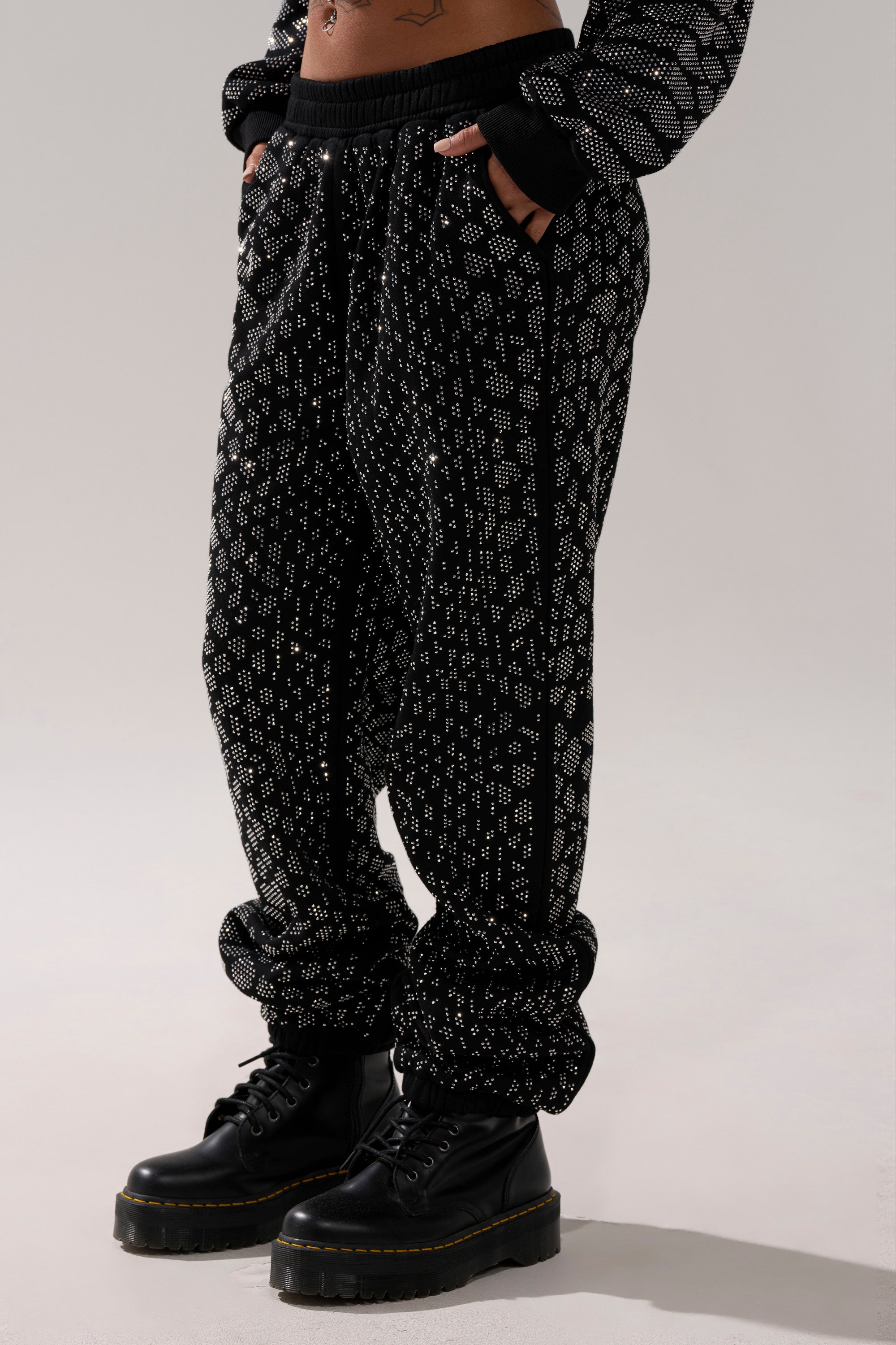 Someone wearing the SNEAKY LITTLE SNAKE WIDE LEG JOGGER and black lace-up boots stands with hands in pockets against a plain light background.