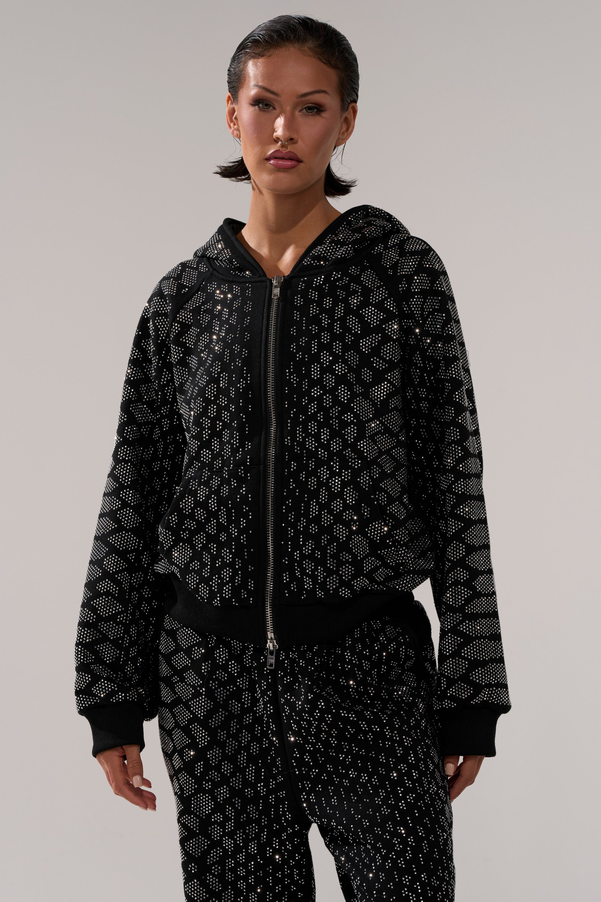 A woman in a black SNEAKY LITTLE SNAKE ZIP UP SWEATSHIRT and matching geometric dotted pants stands against a plain light gray background.
