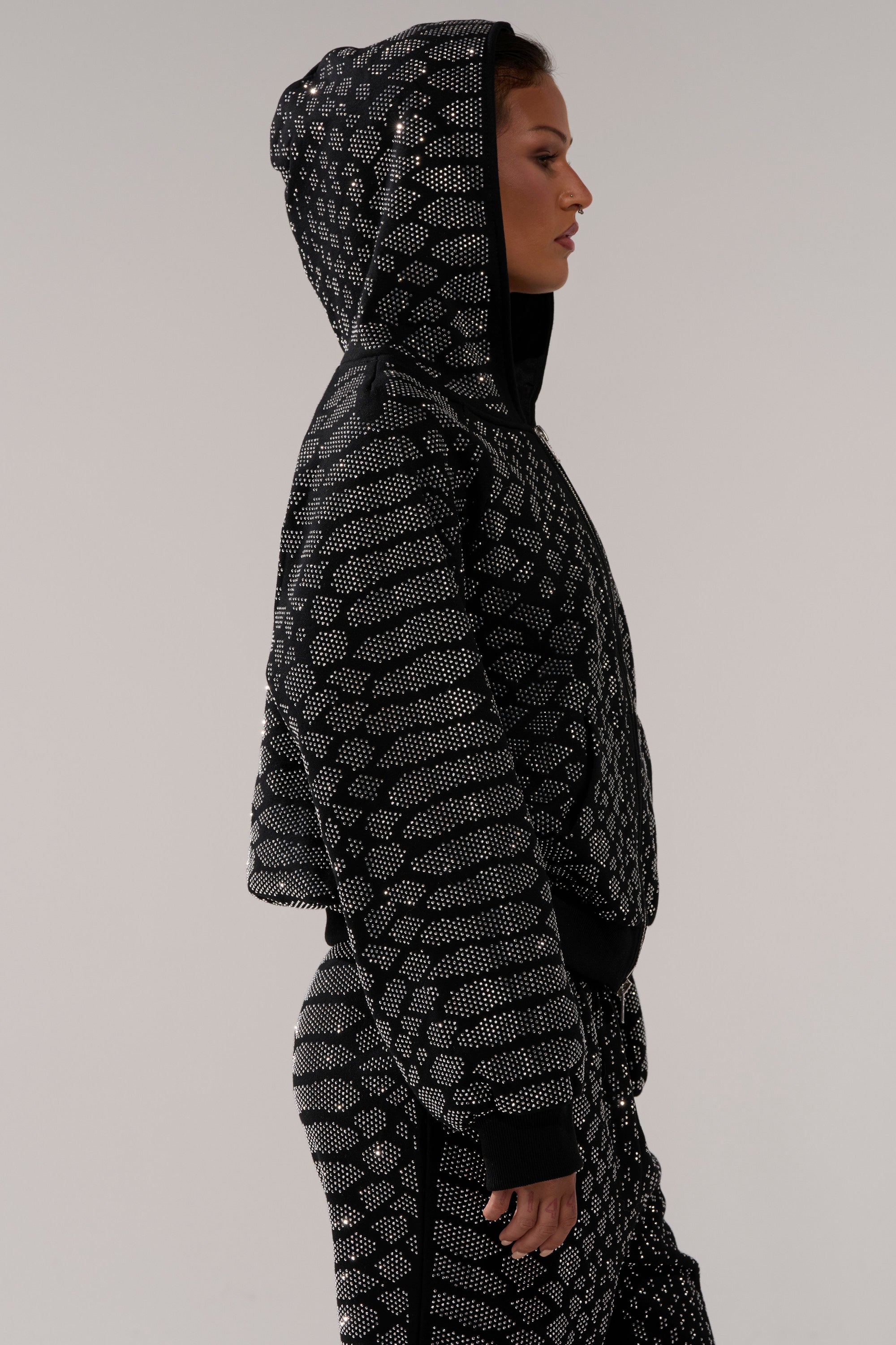 A person in profile wears the SNEAKY LITTLE SNAKE ZIP UP SWEATSHIRT with matching pants, both featuring a dotted geometric pattern, standing against a plain light background.