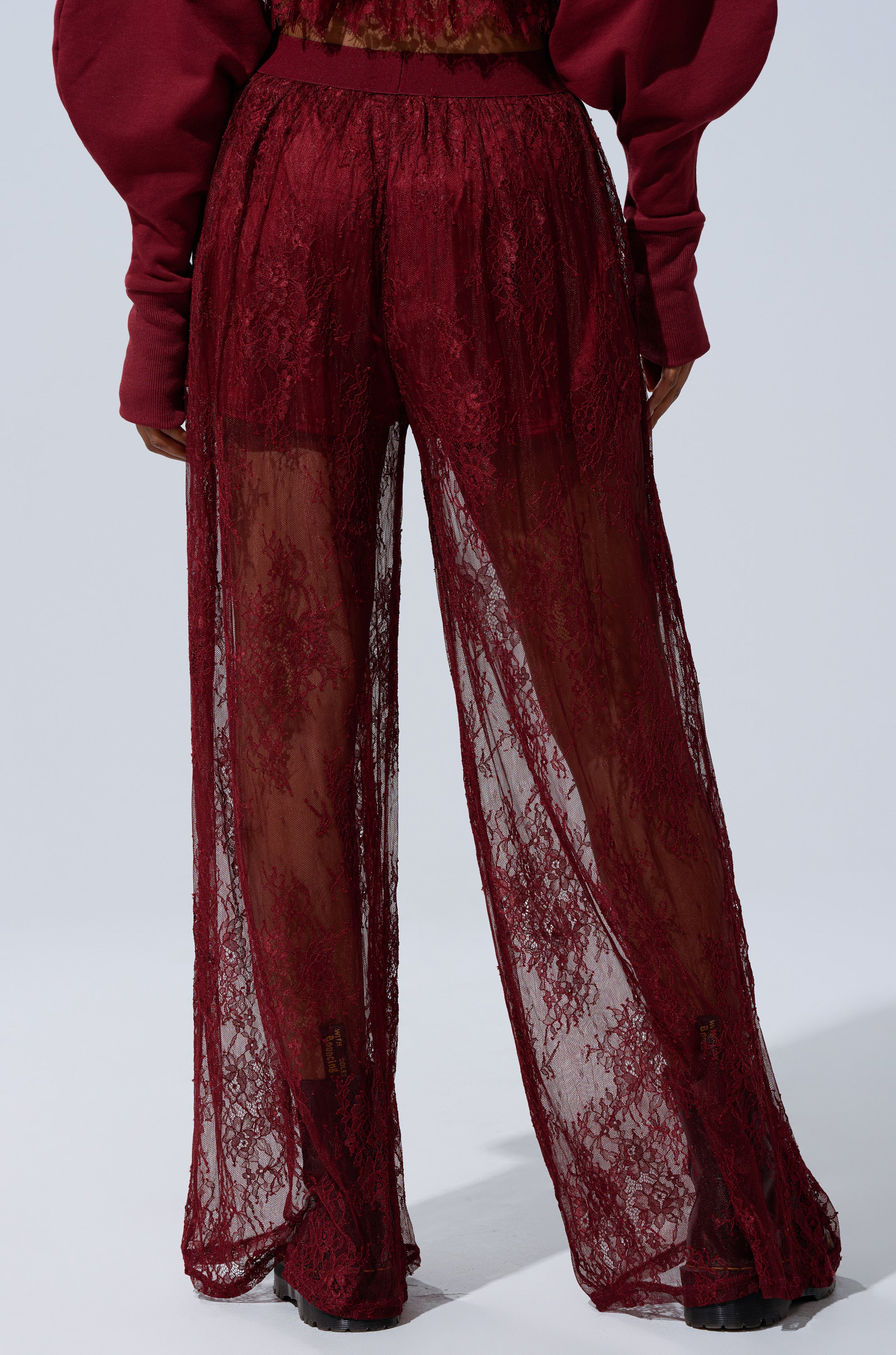 Model wears TOO TRENDY LACE PANTS—high-rise, wide-leg burgundy lace with a sheer, see-through design over matching undergarments—standing against a plain light background with hands by their sides. 4