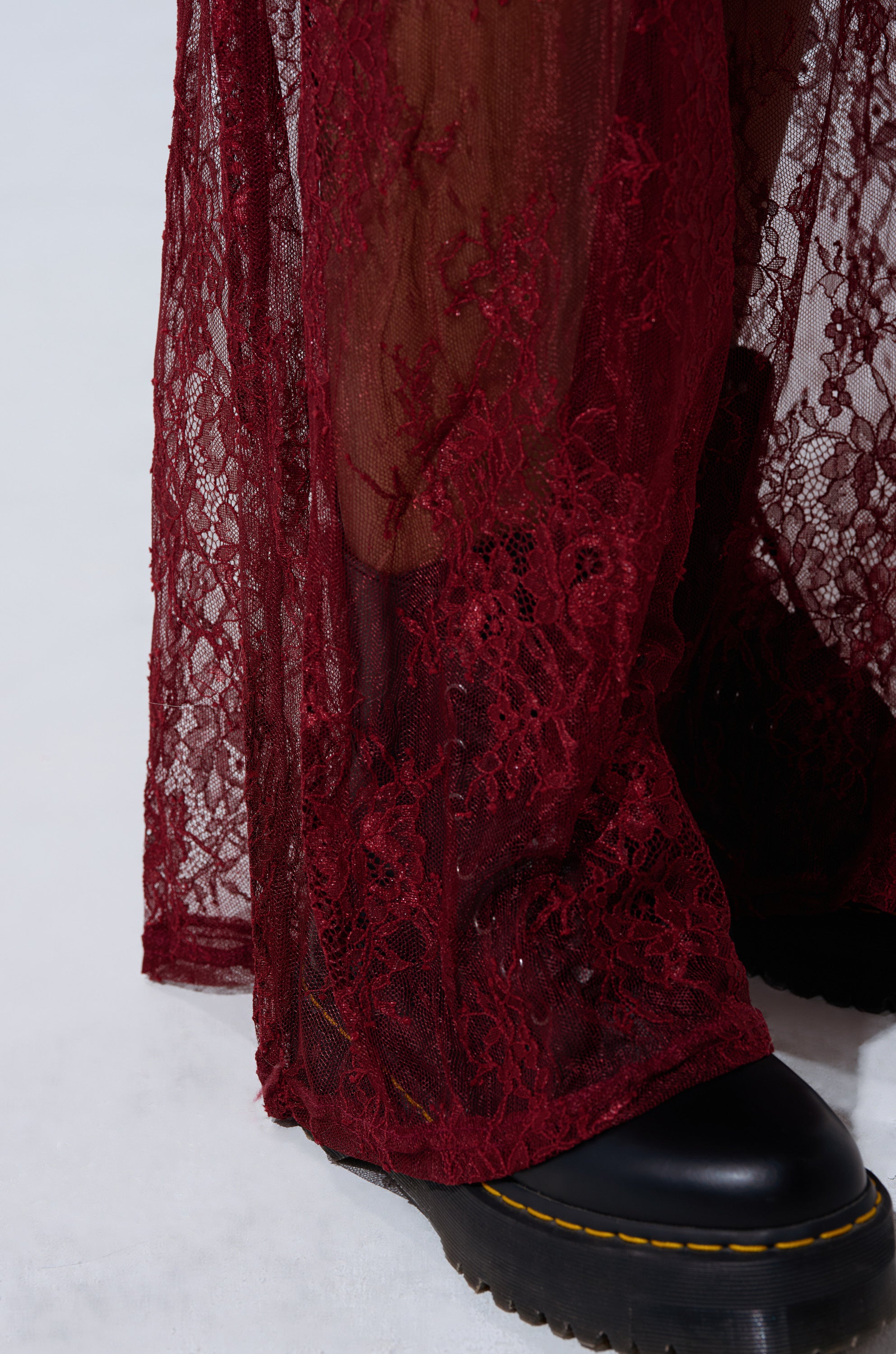 Close-up of a person wearing TOO TRENDY LACE PANTS—sheer, dark red high-rise lace pants that reveal some skin. Styled with black chunky-soled shoes against a plain light background. 7