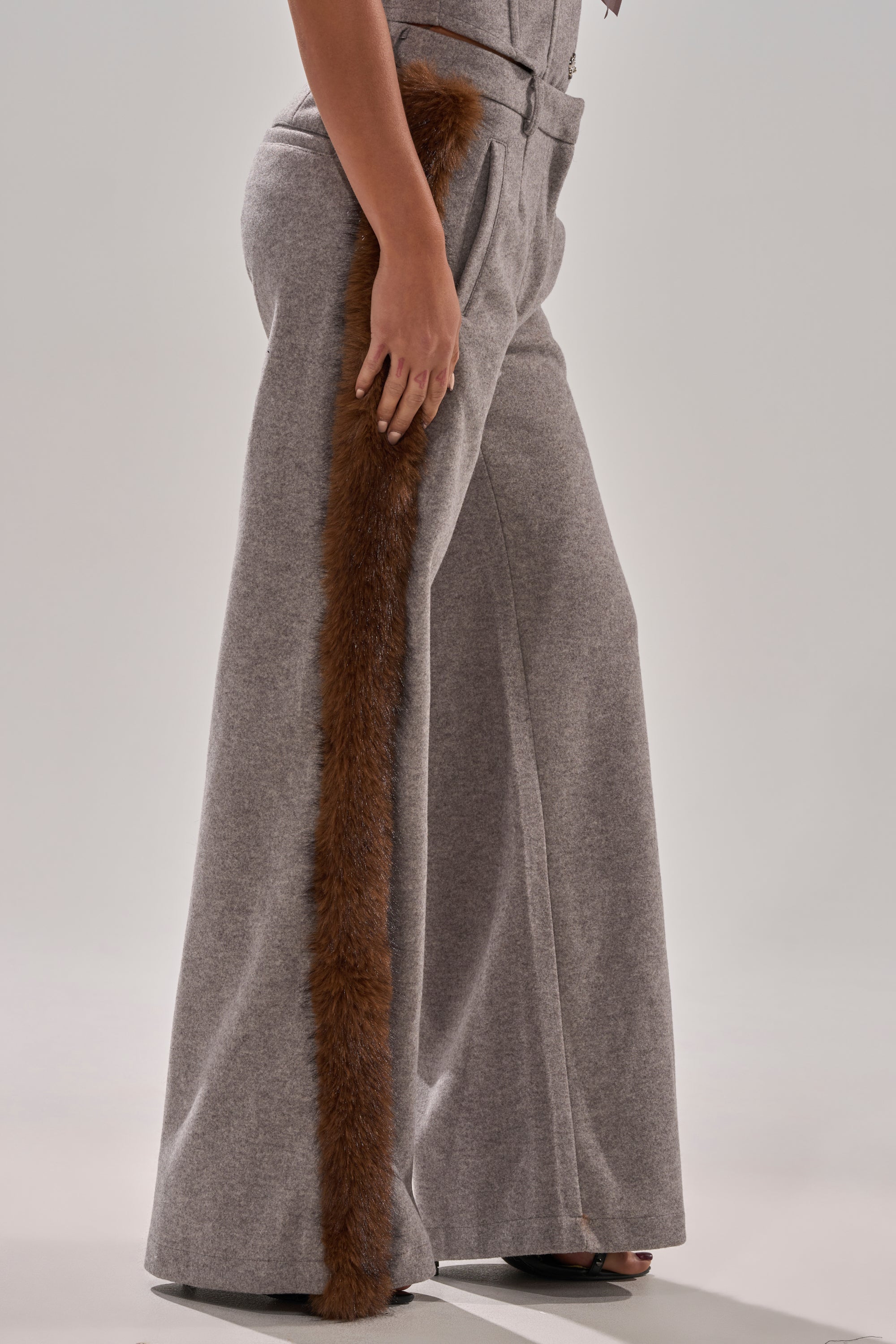 A person wearing the HALLE FUR TRIM WIDE LEG PANT with long brown faux fur trim along the outer seam, standing against a plain light background.