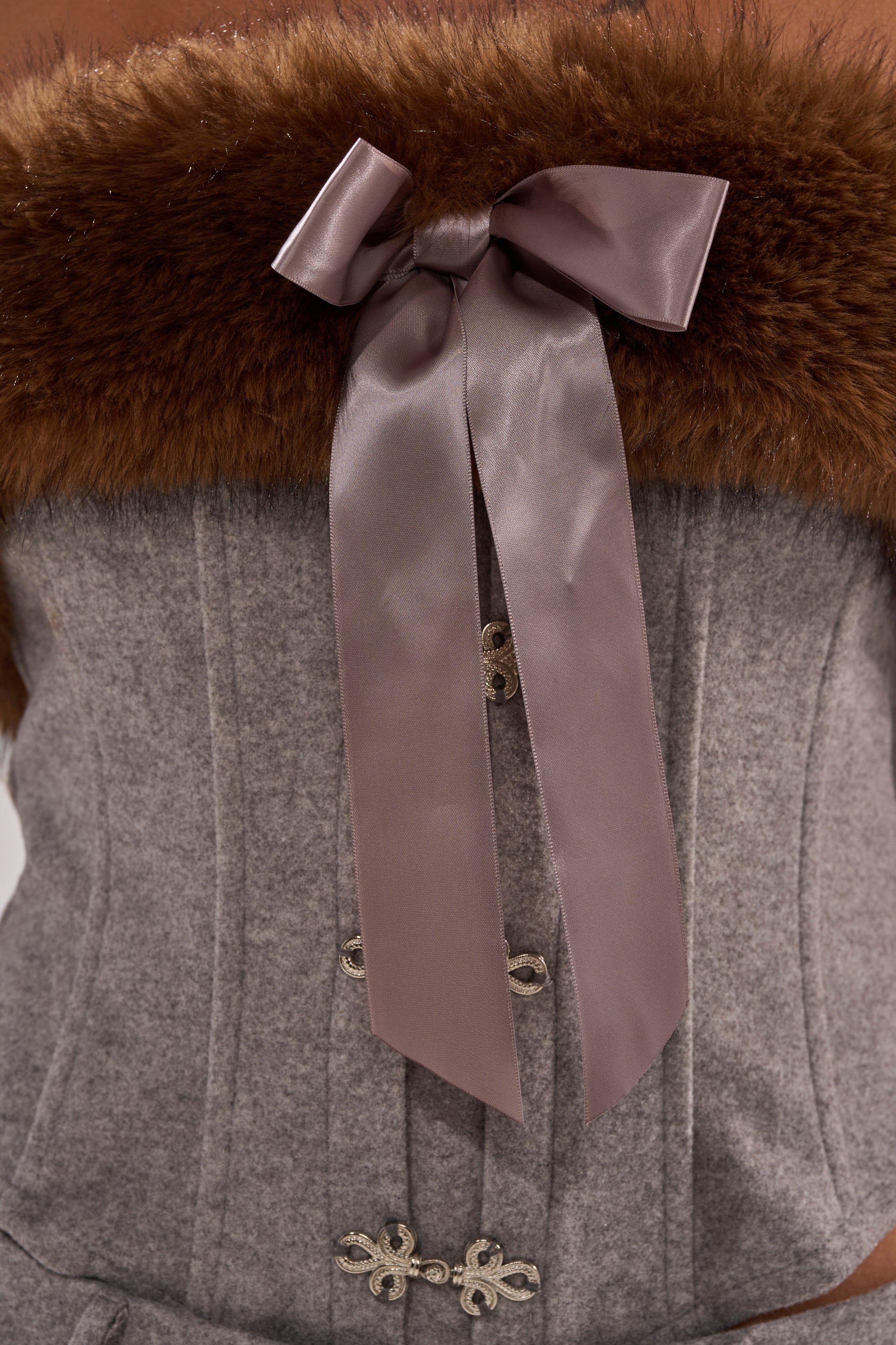 The HALLE FUR TRIM CORSET features a gray fur trim, metal clasps, brown faux fur at the strapless neckline, and a large shiny mauve ribbon bow centered at the front.