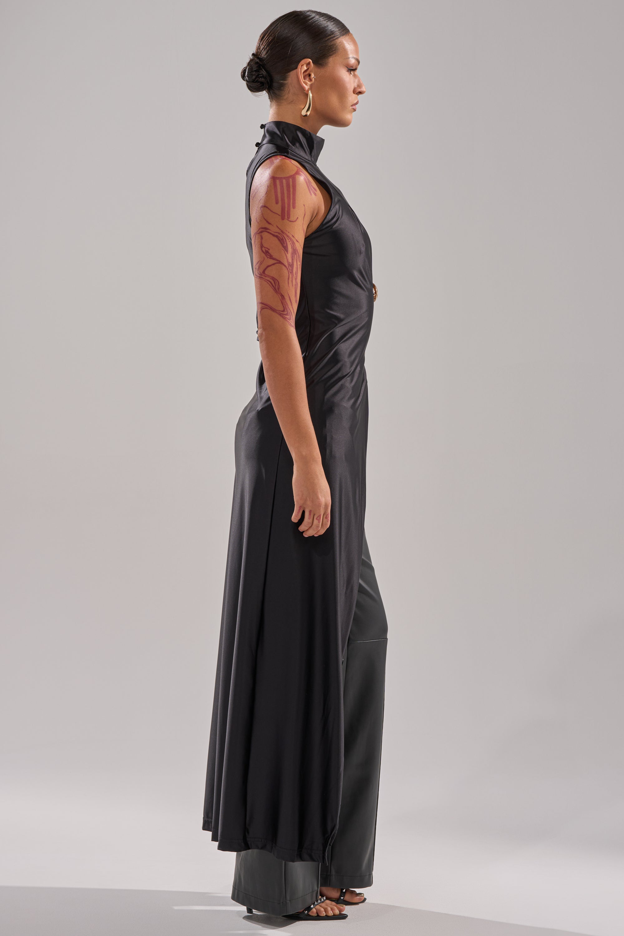 A woman in profile wears the ITS TIME TO CELEBRATE SATIN TURTLE NECK BLOUSE with black pants. Her dark hair is in a neat bun, and her right arm features a bold red design, creating an elegant look for evening wear. 2
