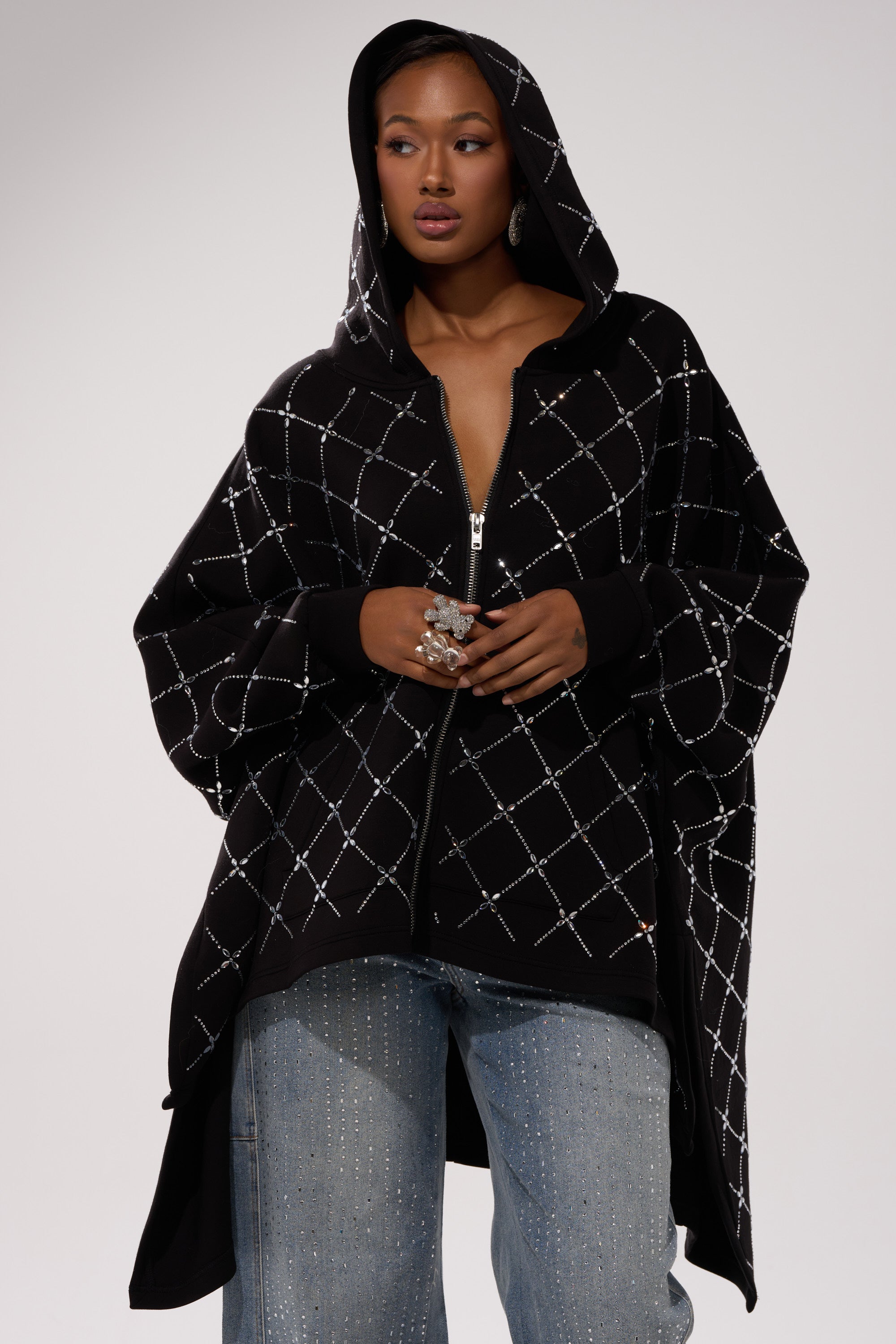 A woman wears the BLING BLING OVERSIZED ZIP UP SWEATSHIRT, a black sweatshirt embellished with silver diamonds—ideal for trendy streetwear layering.