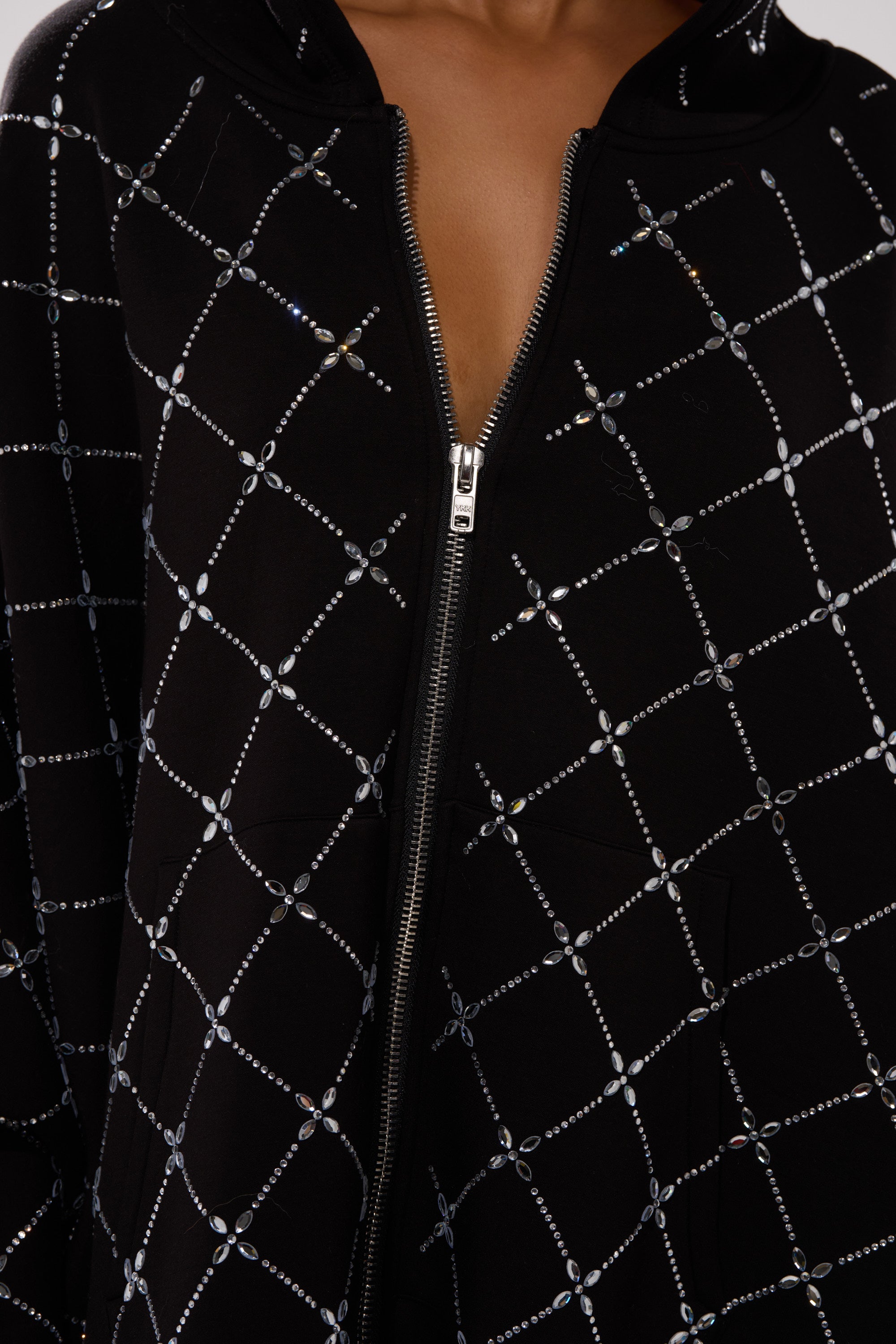 A close-up of the BLING BLING OVERSIZED ZIP UP SWEATSHIRT, a black hoodie with a grid of shiny rhinestones and a partially unzipped silver zipper at the chest, showcasing bold streetwear style.