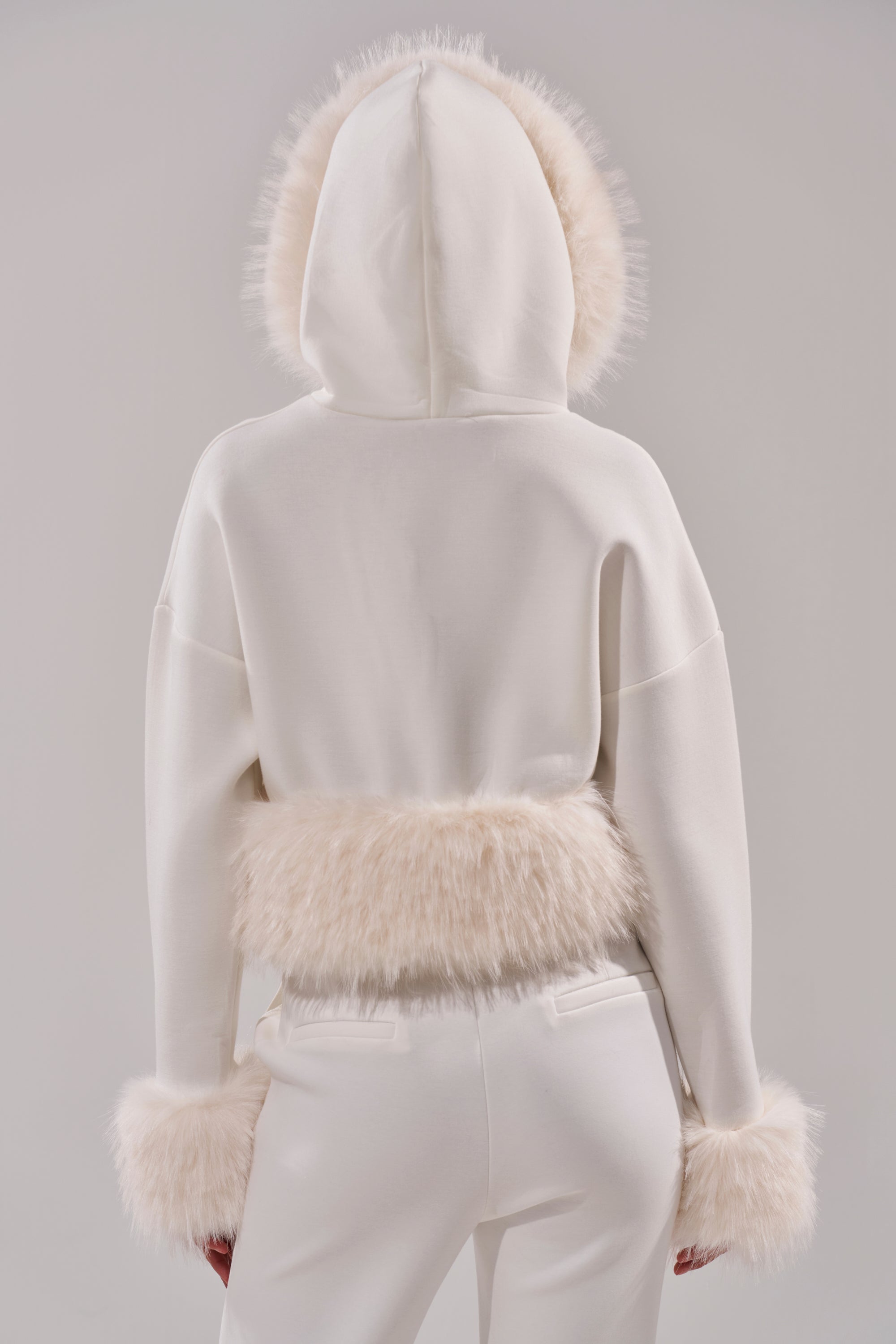 A person is shown from the back in the SNOW WHITE FUR TRIM SWEATSHIRT, featuring plush faux fur on the hood, cuffs, and waistband, paired with white pants against a plain light background. 5