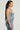 A woman with long, dark hair stands in profile against a plain background. She is wearing the JOLIE RHINESTONE EMBELLISHED DENIM CORSET paired with jeans and accessorized with gold earrings.