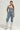 The image showcases a person dressed in the JOLIE RHINESTONE EMBELLISHED DENIM CORSET with matching jeans, complemented by silver knee-high boots and a small purse, creating a chic, cropped silhouette against a plain background.