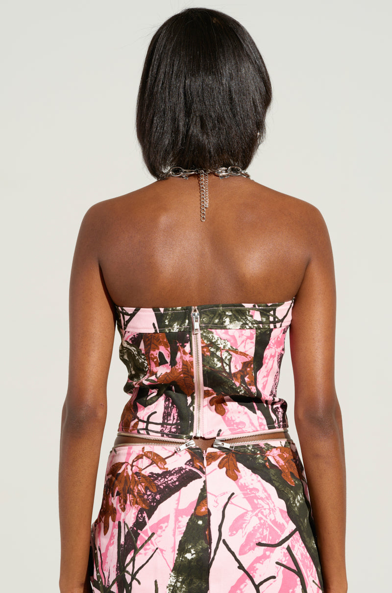 A person with shoulder-length hair is shown from the back, wearing the WEAR IT TWO WAYS TOP OR DRESS, a strapless convertible piece adorned with a pink and brown abstract pattern reminiscent of camouflage. It features a chain strap and a zipper down the back, seamlessly blending style with functionality.
