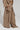 A person dressed in a beige ensemble showcases the AKIRA Label TALK ABOUT ME TROUSER, noted for its wide-leg silhouette and multiple pockets, paired with a loose-fitting top. They complete the look with pointed-toe shoes against a simple, light-colored background.