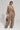 A person dressed in oversized TALK ABOUT ME TROUSER by AKIRA Label, featuring a high-rise design and large pockets, paired with a matching long-sleeved crop top. They carry a glossy bag and accessorize with sunglasses and a chain necklace, set against a plain gray studio backdrop.
