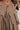 Close-up of a person wearing the TALK ABOUT ME TROUSER by AKIRA Label, showcasing its wide leg silhouette and beige cargo design. The trousers feature two front pockets and zippers, while the high rise style draws attention to a visible belly button piercing. Meanwhile, a geometric tattoo subtly peeks out just above the pants.