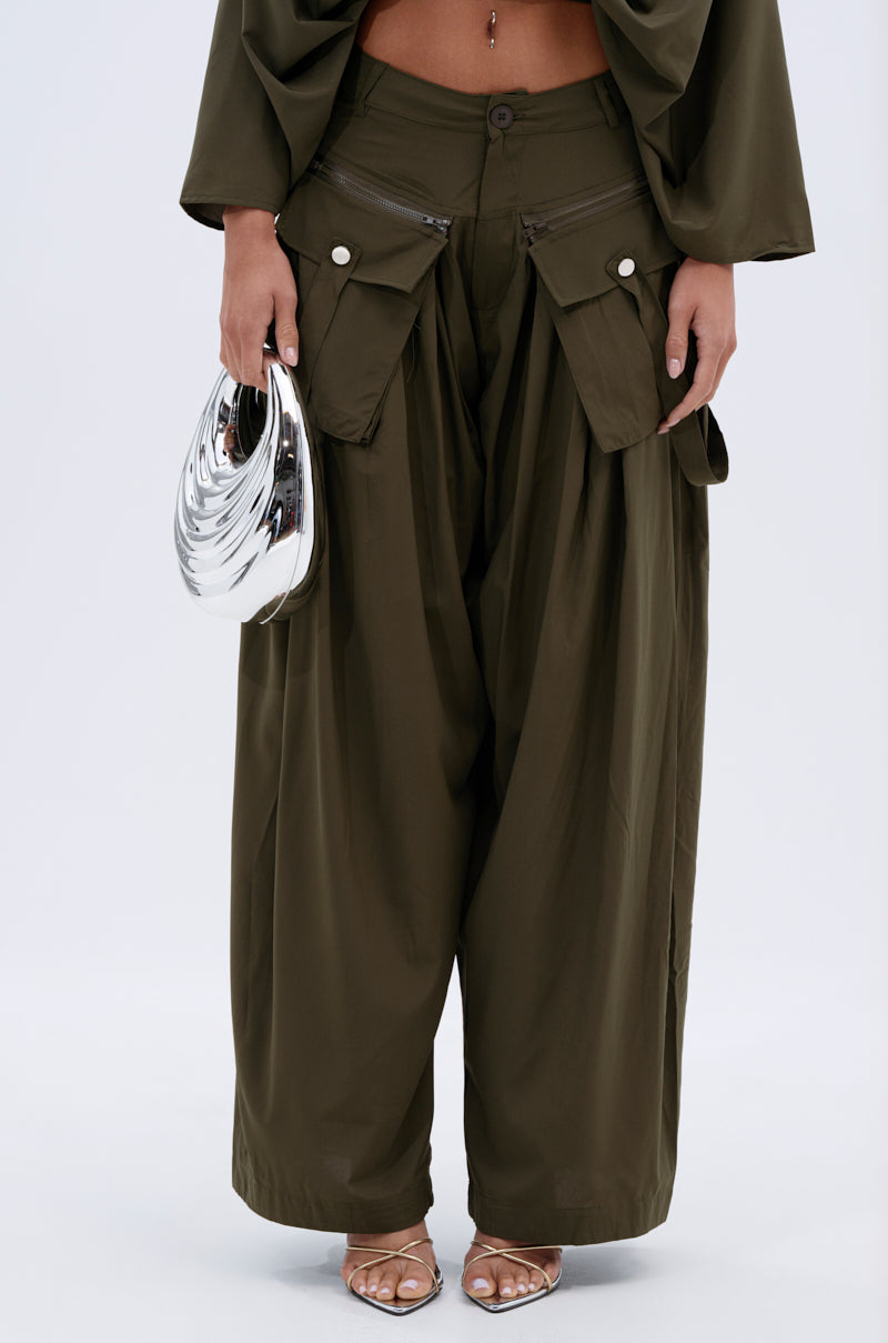 A person wears TALK ABOUT ME TROUSER high-rise wide-leg pants with large pockets, a matching top that reveals their midriff, beige heeled sandals, and carries a shiny silver metallic handbag. 2